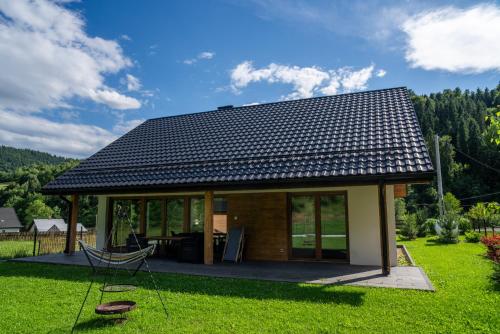 a small house with a black roof on a green lawn at Domek na Duzynie in Ochotnica Górna
