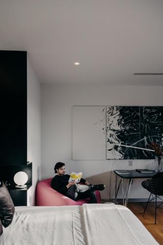 a man sitting on a red couch reading a book at Tá Hotel de diseño in Querétaro