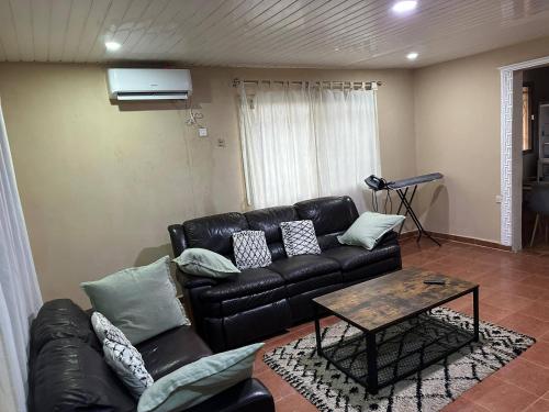 a living room with a black leather couch and a table at Full AirCon- 3Bed Villa- A c- WiFi- HotWater in Freetown