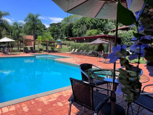 a pool with a table and chairs and an umbrella at Hotel Fazenda Vale Alvorada in Cascavel