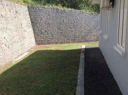 a backyard with a brick wall and a grass yard at Les terrasses de Maëlle II in Rivière-Salée