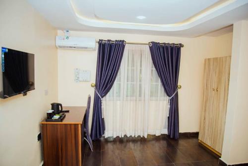 a room with purple curtains and a desk and a television at Ascot Tulip Hotel in Enugu