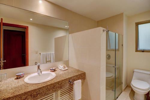 a bathroom with a sink and a toilet and a mirror at Palmar del Sol by Riviera Maya Suites in Playa del Carmen