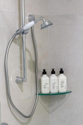 a shower with three shampoo bottles on a shelf at Stylish 3BR Escape Parking & Modern Living in Christchurch