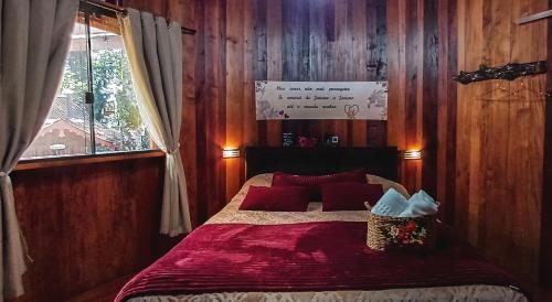 a bedroom with a bed with red pillows and a window at Chalé Temático em Pipa de Vinho - Parada da Pipa Chalés in Canela