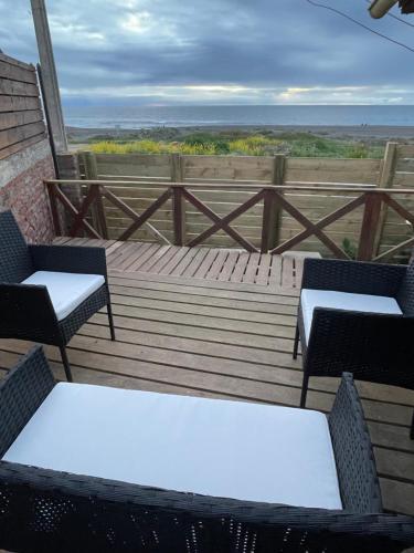 deux chaises et tables sur une terrasse en bois avec l'océan dans l'établissement Beach house Pichilemu - Casa frente al mar, à Pichilemu