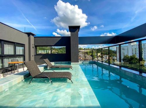 a swimming pool with two chairs and a building at Loft Moderno no Centro de Blumenau in Blumenau