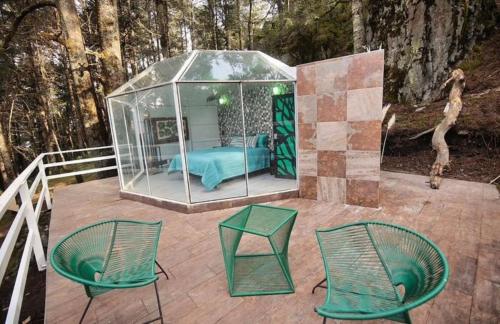 a glass house with a bed and chairs on a deck at Glampina in Huixquilucan