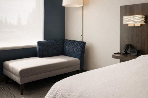 a room with a chair and a bed and a window at Holiday Inn Express & Suites Fresno Airport by IHG in Fresno