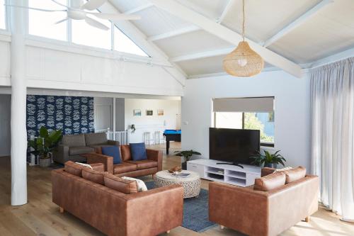 a living room with couches and a flat screen tv at Barefoot Bungalow - Beachfront Byron Bay in Byron Bay
