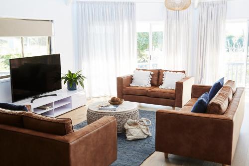a living room with two couches and a flat screen tv at Barefoot Bungalow - Beachfront Byron Bay in Byron Bay