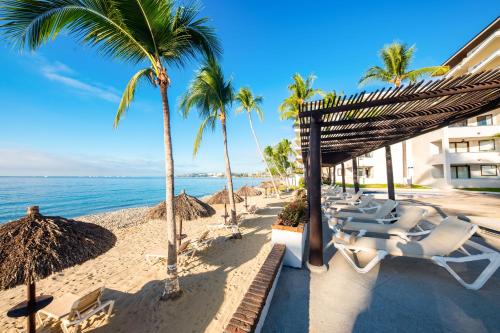 a beach with a bunch of chairs and palm trees at Vista Vallarta All Suites On The Beach in Bucerías
