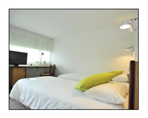 a bedroom with two white beds with a green pillow at Kyriad Châlons-En-Champagne - Saint-Martin in Châlons-en-Champagne