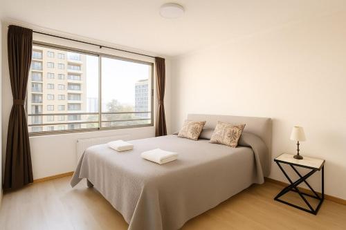 a white bedroom with a bed and a large window at Steps from the subway and Free Parking in Santiago