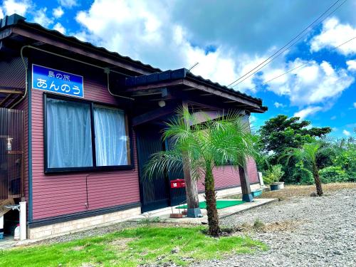a pink house with a palm tree in front of it at 島の旅あんのう in Nishinoomote