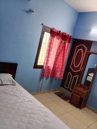 a bedroom with a bed with a red curtain and a window at Uddish Residency in Virāmpattinam