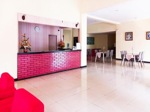 a lobby with a red wall and tables and chairs at Hotel Palem Sari Syariah Batu RedPartner in Punten