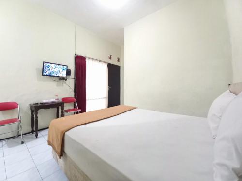 a bedroom with a bed and a table and a television at Hotel Palem Sari Syariah Batu RedPartner in Punten