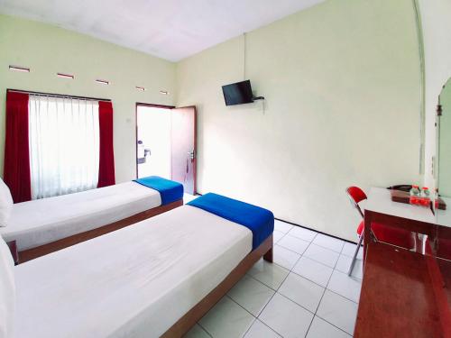 a bedroom with two beds and a desk and a television at Hotel Palem Sari Syariah Batu RedPartner in Punten