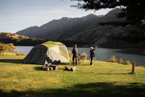 two people standing next to a tent next to a lake at Rent-A-Tent - Hire camping gear in Auckland