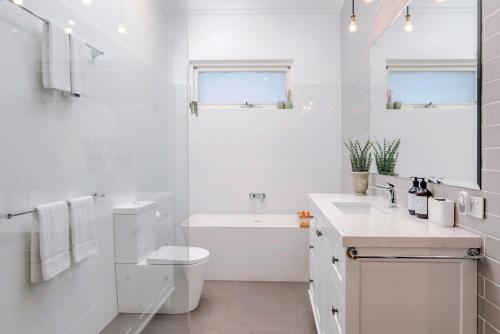 a white bathroom with a tub and a toilet and a sink at Henley Beach House - Luxury by the Sea in Henley Beach