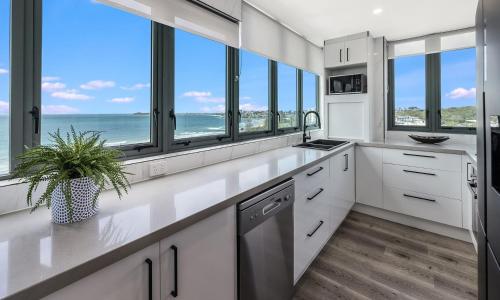 a kitchen with white cabinets and windows and the ocean at Sunny Coast Escapes - Maroochydore in Maroochydore