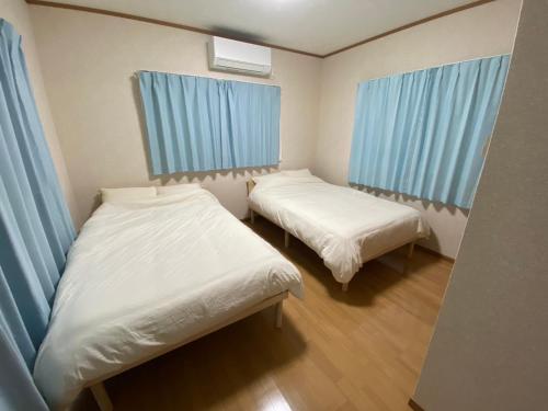 two beds in a small room with blue curtains at ゲストハウスえらぶー7 in Wadomari