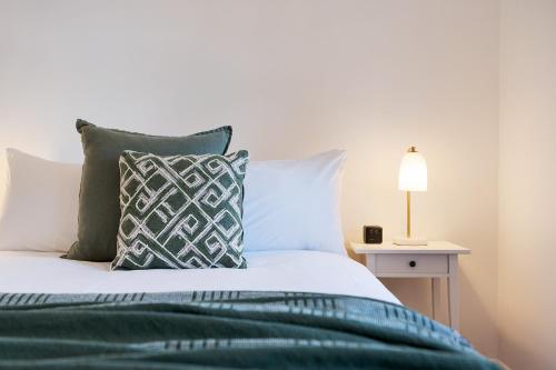 a bed with green and white pillows and a lamp at Victorian Hilltop Retreat - Firepit & Sunset Views in Castlemaine