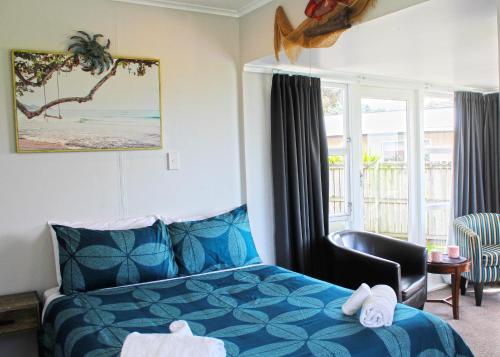 - une chambre avec un lit bleu, une chaise et une fenêtre dans l'établissement Waitangi Beach Unit A, à Paihia