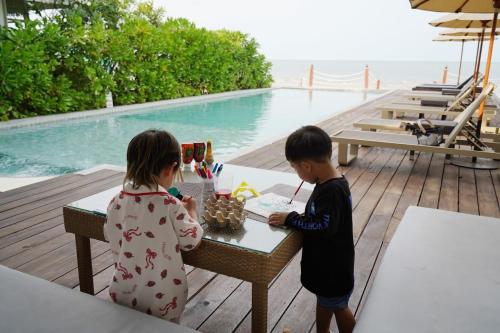 two children standing at a table next to a pool at De Chaochom Hua Hin in Hua Hin