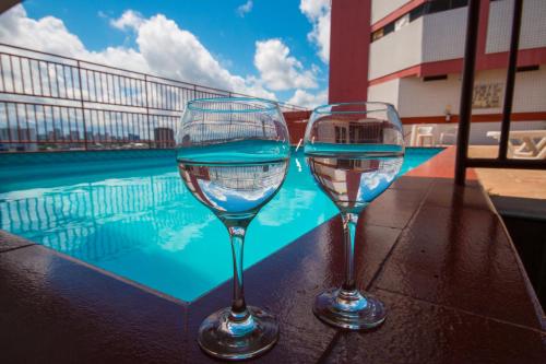 dos copas de vino sentadas en una mesa junto a una piscina en Taj Mahal Hotel en Manaos