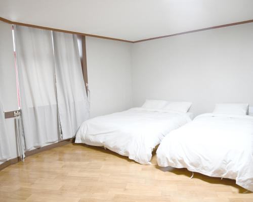 two beds in a room with white walls and wood floors at Sorak Hostel in Sokcho