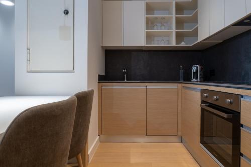 a kitchen with white cabinets and a sink and two chairs at Zepterme Spa&Wellness Luxury Apartments member of Zepter hotels in Vrnjačka Banja