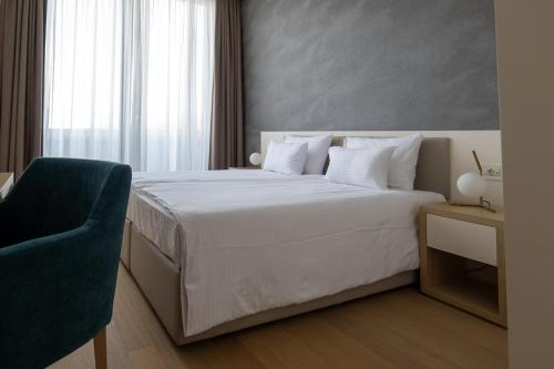 a bedroom with a white bed and a blue chair at Zepterme Spa&Wellness Luxury Apartments member of Zepter hotels in Vrnjačka Banja