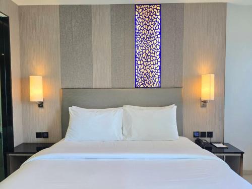 a bedroom with a bed with white pillows and a window at THE TJ HOTEL Pattaya in Jomtien Beach