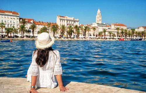 a woman sitting on a ledge looking at the water at Bora bora Apartment in Kaštela
