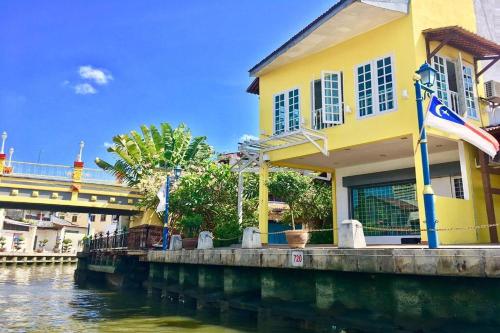 a yellow building next to a river with a bridge at Sleepy Nomad Hostel in Melaka