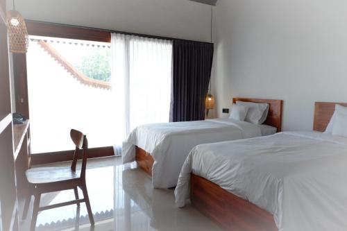 a bedroom with two beds and a chair and a window at Ginantary Cottages in Uluwatu