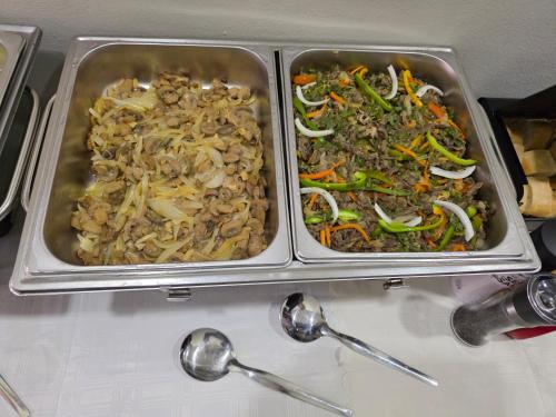 two trays of food sitting on a table with spoons at White Garden Hotel in Maputo