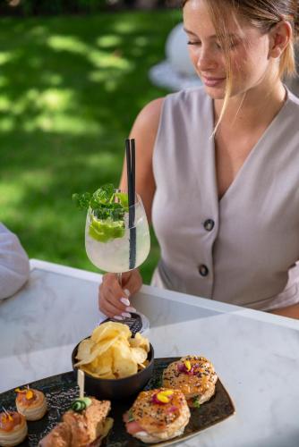 a woman holding a drink and a plate of food at Bolina Suite & Spa in Milano Marittima