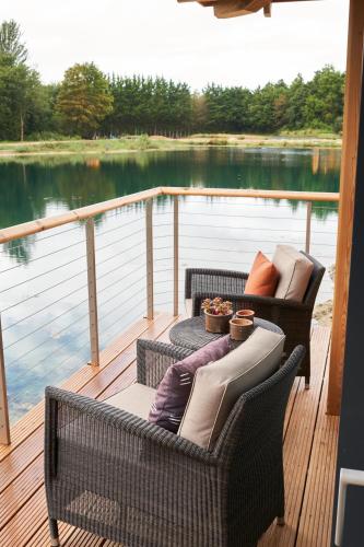two wicker chairs and a table on a deck with water at The Lakes By YOO in Lechlade