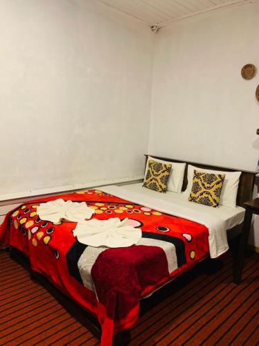a bedroom with a large bed with a red and white blanket at SHADOW MASK BUNGALOW in Pattipola