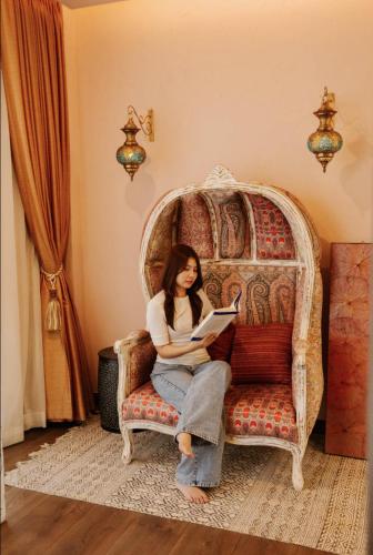 a woman sitting on a chair reading a book at Palm Villa - Award Winning Modern Luxury & Exclusive Villa in Chiang Mai