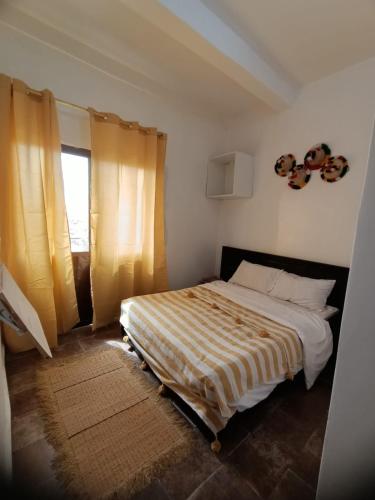 a bedroom with a bed with a striped comforter and a window at Tildi surf house in Imsouane