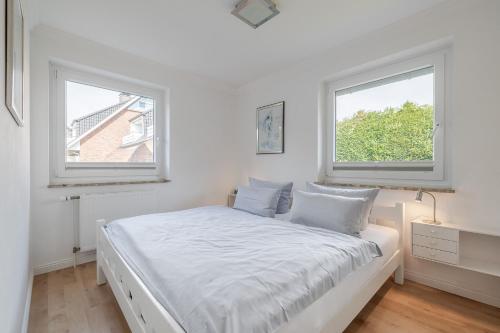 a white bedroom with two windows and a bed at Meer in Süderende