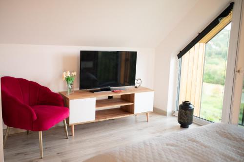 a living room with a television and a red chair at StyLove Domki 1 in Kluszkowce