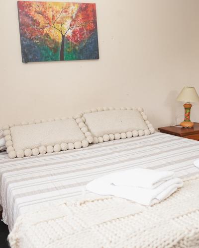 a bed with white sheets and a painting on the wall at Hospedaje La Pasada in Tafí del Valle