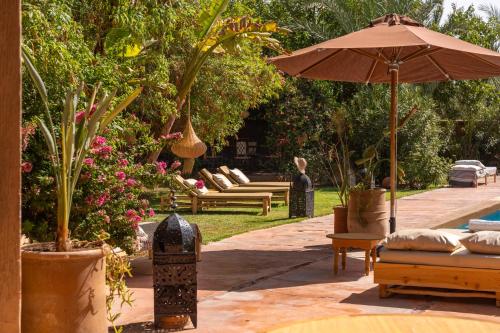 a patio with benches and an umbrella in a garden at Hacienda de Julie in Sraïri
