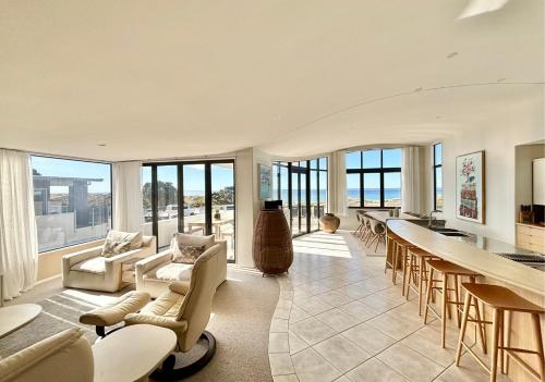 an open living room with a bar and chairs and windows at Supreme on Marine - Beachfront! in Mount Maunganui