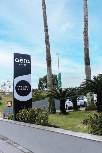 a sign in front of a parking lot with palm trees at Aéra São José Floripa in São José